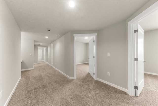 corridor with baseboards, light colored carpet, and a textured ceiling