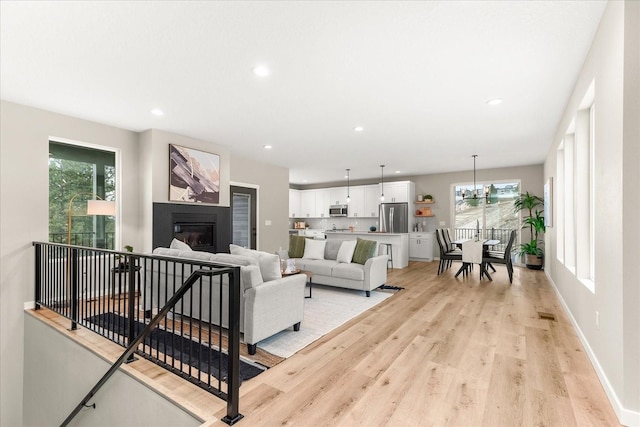 living area with a glass covered fireplace, recessed lighting, baseboards, and light wood-style floors