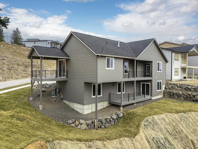 rear view of house with a balcony, cooling unit, a yard, and roof with shingles