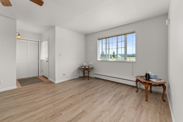 spare room featuring a baseboard heating unit, wood finished floors, baseboards, and a ceiling fan