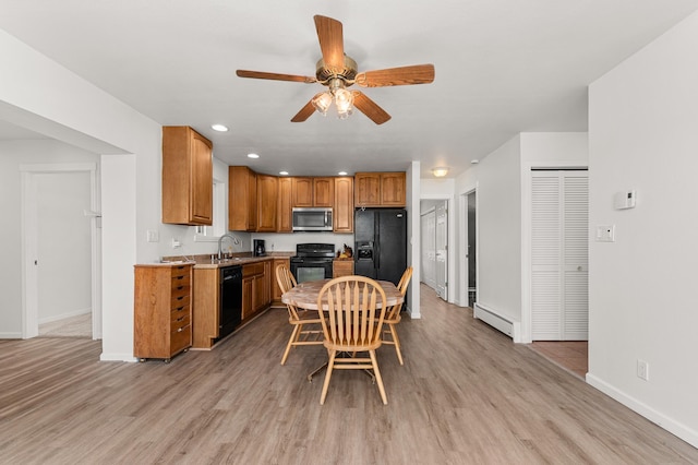 kitchen with a sink, a baseboard heating unit, black appliances, and light wood-style flooring