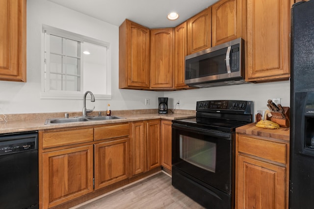 kitchen with brown cabinetry, a sink, black appliances, light countertops, and light wood-style floors