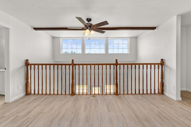 empty room with beam ceiling, plenty of natural light, baseboards, and wood finished floors