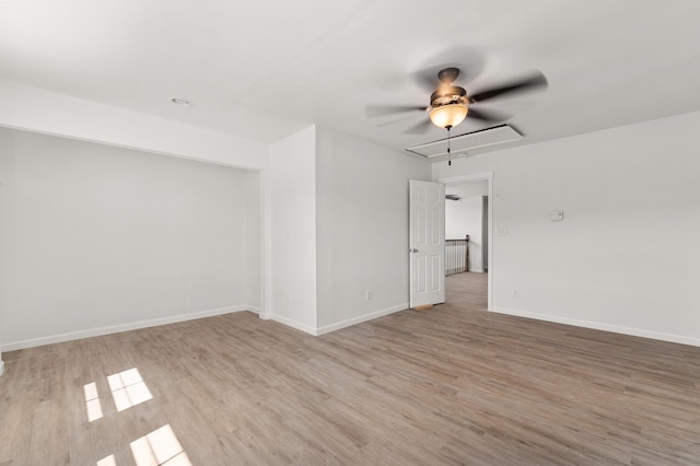 spare room with attic access, light wood-style flooring, baseboards, and ceiling fan