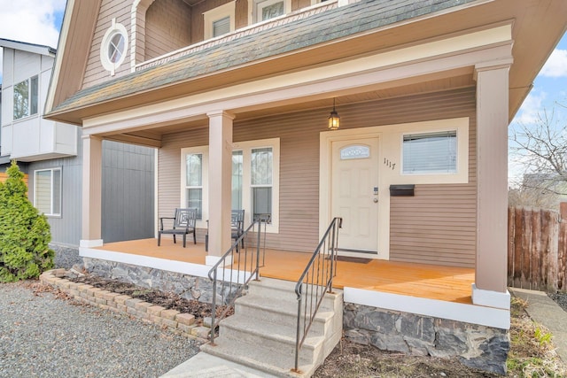 doorway to property with a porch, a shingled roof, and fence