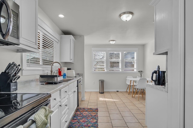 kitchen with baseboards, light countertops, light tile patterned flooring, white cabinetry, and a sink