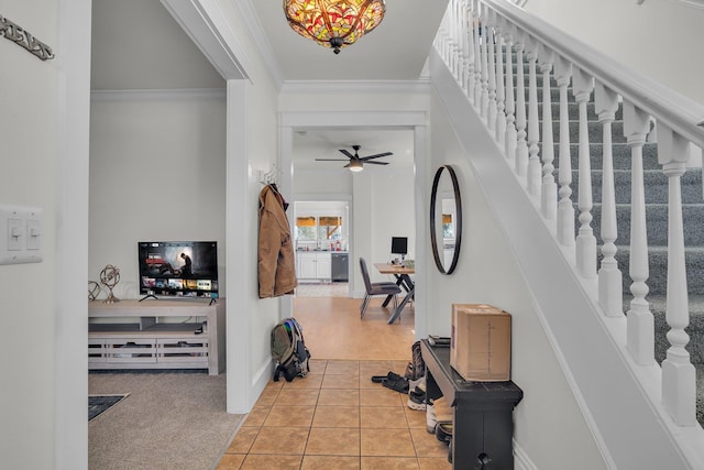 foyer with ornamental molding, stairway, light tile patterned flooring, light colored carpet, and ceiling fan