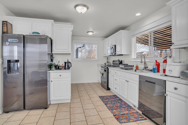 kitchen with light countertops, light tile patterned floors, stainless steel appliances, white cabinetry, and a sink