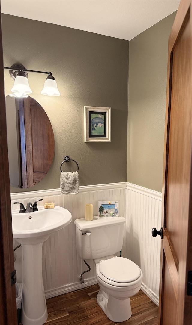 bathroom with a sink, toilet, wood finished floors, and wainscoting