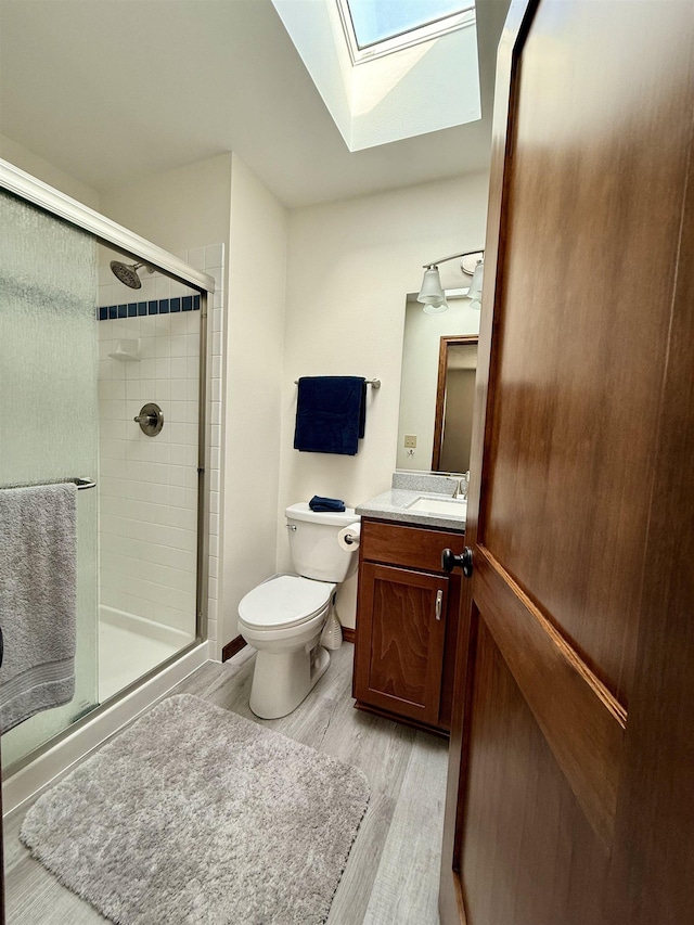 full bath featuring vanity, wood finished floors, a skylight, a stall shower, and toilet