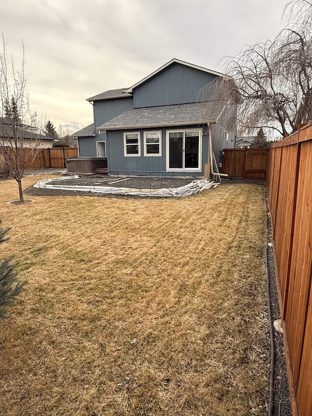 back of house featuring a yard, a fenced backyard, roof with shingles, and a hot tub