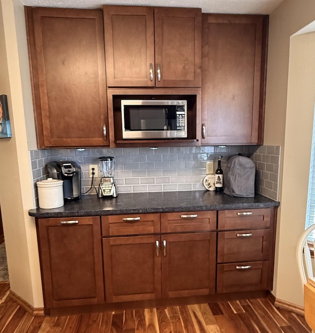 bar featuring stainless steel microwave, dark wood-style floors, baseboards, and backsplash