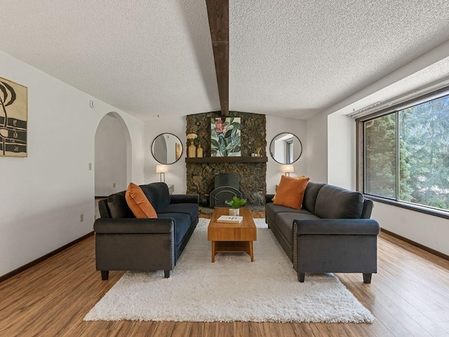 living area with arched walkways, beamed ceiling, baseboards, and wood finished floors