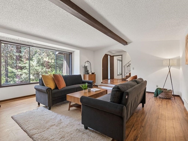 living room featuring wood finished floors, arched walkways, stairs, a textured ceiling, and beamed ceiling