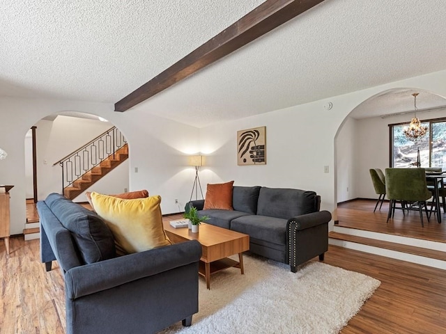 living area with beamed ceiling, stairway, wood finished floors, and arched walkways