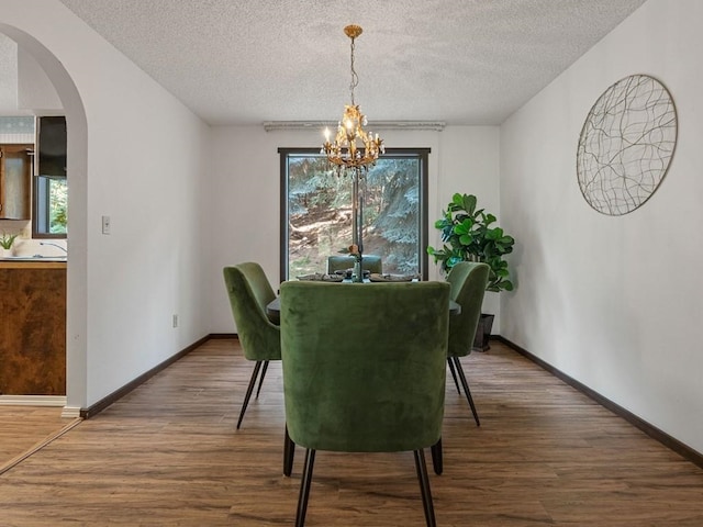 dining room with arched walkways, a textured ceiling, an inviting chandelier, and wood finished floors