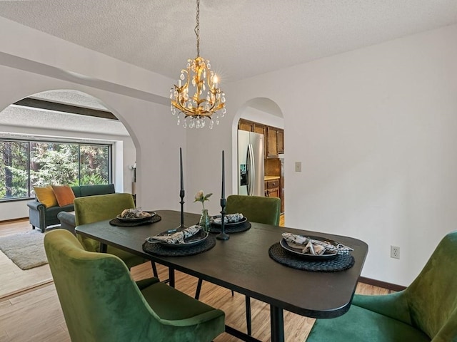 dining room featuring a textured ceiling, arched walkways, light wood finished floors, and a chandelier