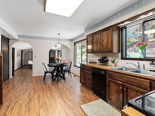 kitchen featuring light wood finished floors, wallpapered walls, arched walkways, a sink, and black appliances