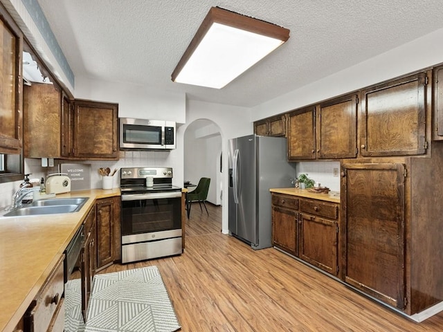 kitchen with arched walkways, a sink, light countertops, dark brown cabinets, and appliances with stainless steel finishes