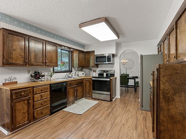 kitchen with dark brown cabinets, light wood-type flooring, light countertops, arched walkways, and stainless steel appliances