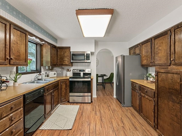 kitchen featuring dark brown cabinetry, light wood-style floors, arched walkways, stainless steel appliances, and a sink