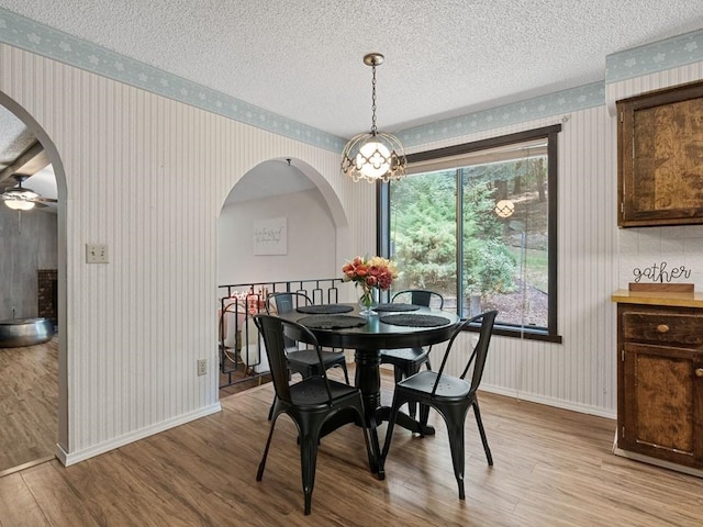 dining space with baseboards, wallpapered walls, arched walkways, light wood-style floors, and a textured ceiling