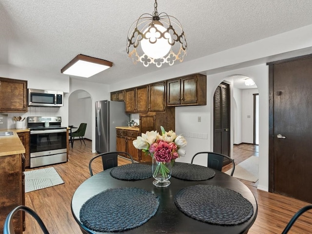 dining area featuring a textured ceiling, arched walkways, and light wood-type flooring