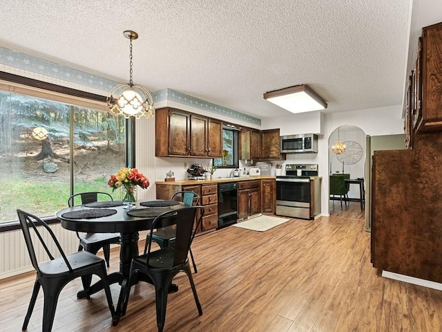 kitchen with dark brown cabinets, light countertops, light wood-style flooring, arched walkways, and stainless steel appliances