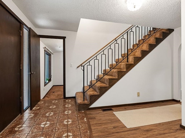 stairs featuring visible vents, baseboards, a textured ceiling, and wood finished floors