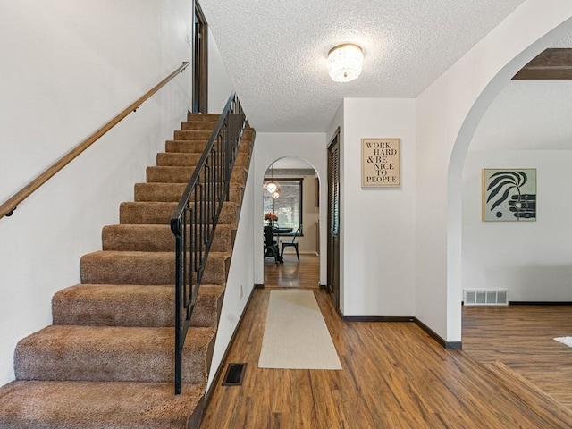 stairs featuring arched walkways, visible vents, a textured ceiling, and wood finished floors