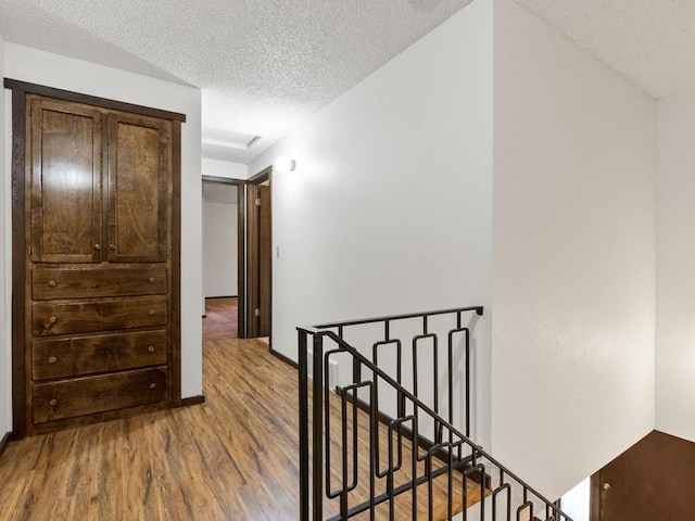 hallway with wood finished floors, attic access, an upstairs landing, and a textured ceiling