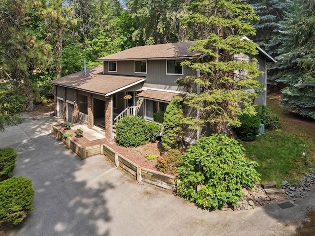 view of front of house featuring brick siding, driveway, an attached garage, and a forest view