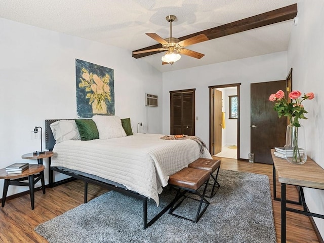 bedroom featuring a textured ceiling, vaulted ceiling, wood finished floors, and a wall mounted AC