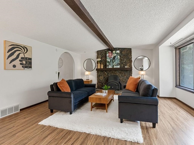 living area with visible vents, arched walkways, light wood-style floors, and beam ceiling