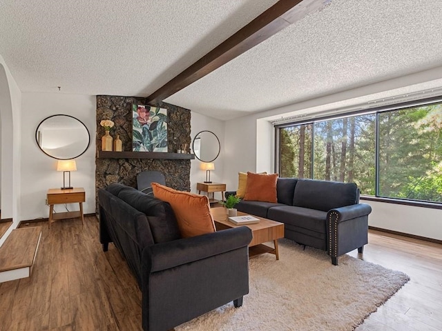 living area with a fireplace, beamed ceiling, wood finished floors, and a textured ceiling