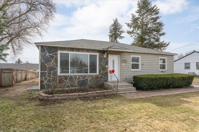 view of front facade featuring a front lawn, fence, and stone siding