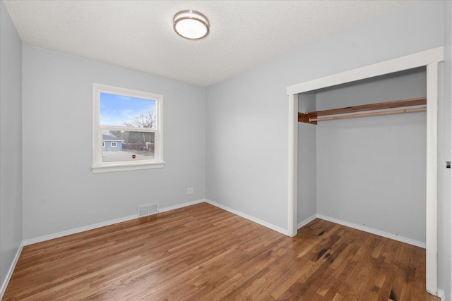 unfurnished bedroom featuring a closet, visible vents, baseboards, and wood finished floors