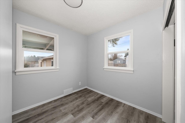 unfurnished room featuring dark wood finished floors, baseboards, visible vents, and a textured ceiling