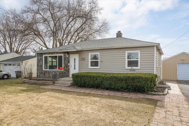 view of front of house with a detached garage, roof with shingles, a front yard, a chimney, and an outdoor structure