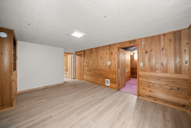 empty room with visible vents, wood finished floors, baseboards, and wood walls