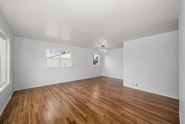 empty room with a notable chandelier, wood finished floors, and visible vents