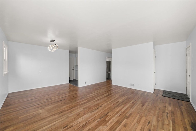 unfurnished living room with a notable chandelier, wood finished floors, and visible vents