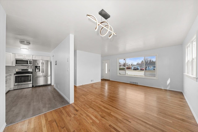 kitchen with visible vents, light wood-style flooring, stainless steel appliances, white cabinets, and tasteful backsplash