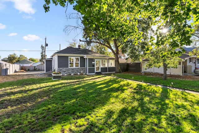 view of front facade featuring a chimney, stone siding, fence private yard, and a front lawn