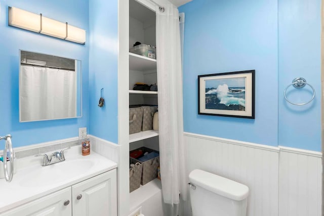 bathroom featuring a shower with shower curtain, vanity, toilet, and wainscoting