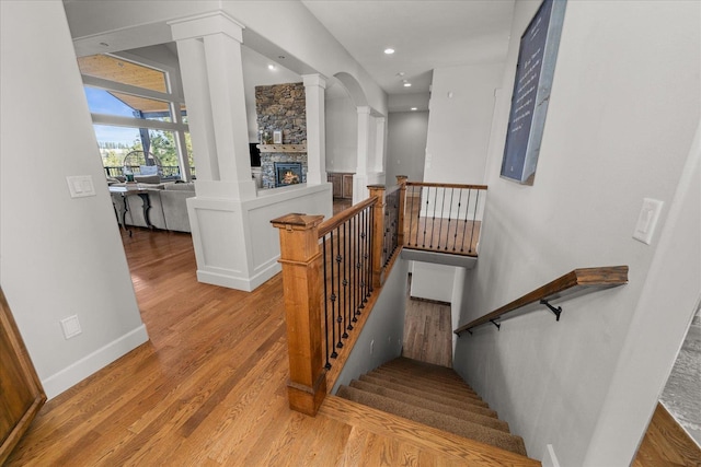 stairway featuring wood finished floors, baseboards, ornate columns, recessed lighting, and a stone fireplace