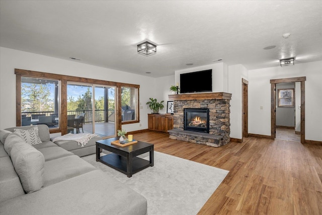 living area featuring visible vents, baseboards, light wood-style flooring, a stone fireplace, and a textured ceiling