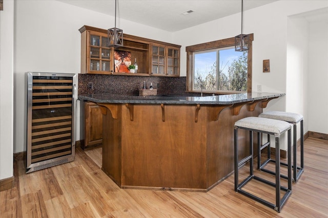 bar with tasteful backsplash, wine cooler, pendant lighting, indoor wet bar, and light wood-style floors