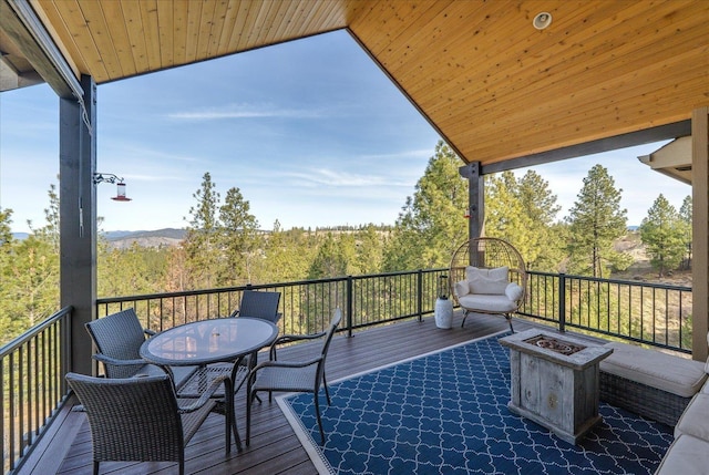 deck with a wooded view, a fire pit, and outdoor dining area