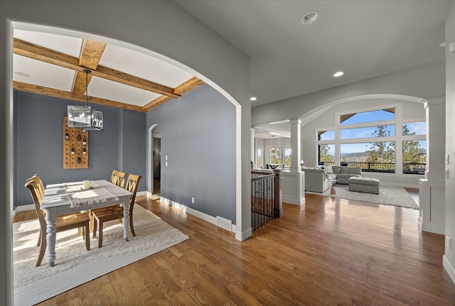 dining area with a notable chandelier, coffered ceiling, wood finished floors, arched walkways, and ornate columns